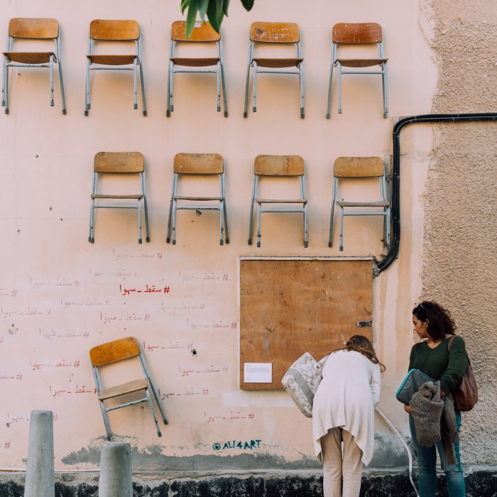 Photograph of two women looking at some street art of chairs mounted on a wall.