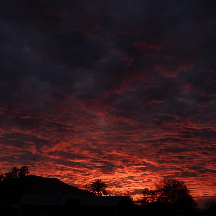 Photograph of a sunset sky coloured orange and purple and filled with rippling clouds.