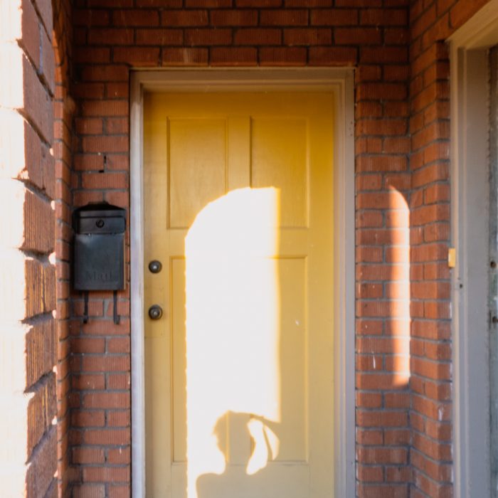 Photograph of a person's silhoutte as they take a photo in front of a yellow door surrounded by red bricks.