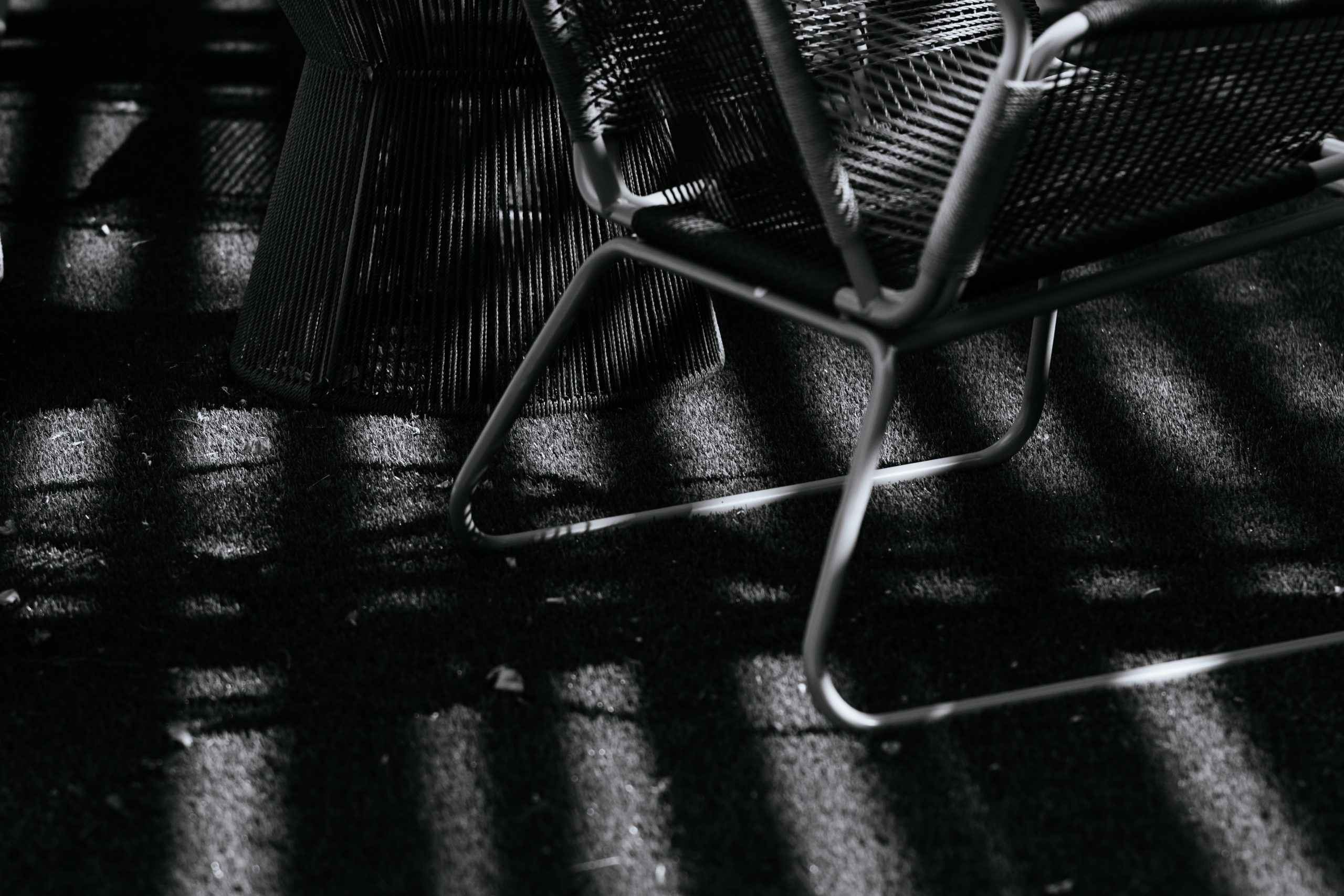 Black and white photo of high contrast light and shadow of patio furniture and astro turf.