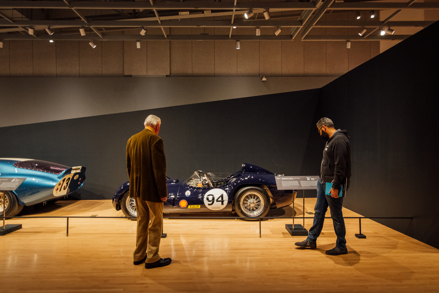 Photo of 2 people looking at a classic car.