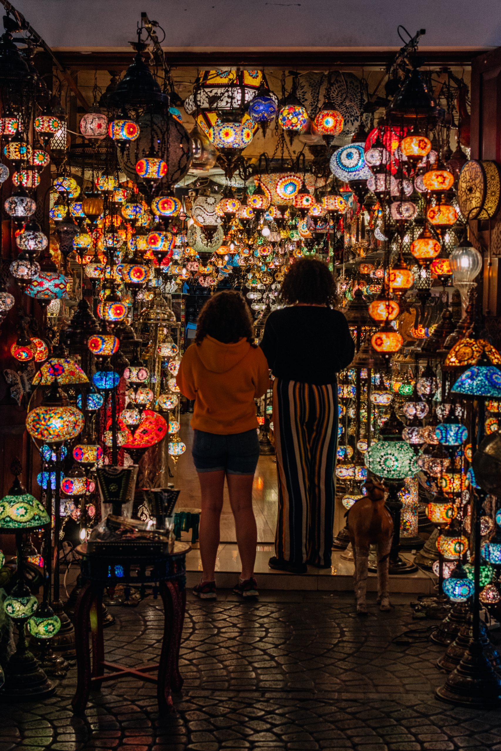 Photo of the back of two people surrounded by hanging Moroccan lights.