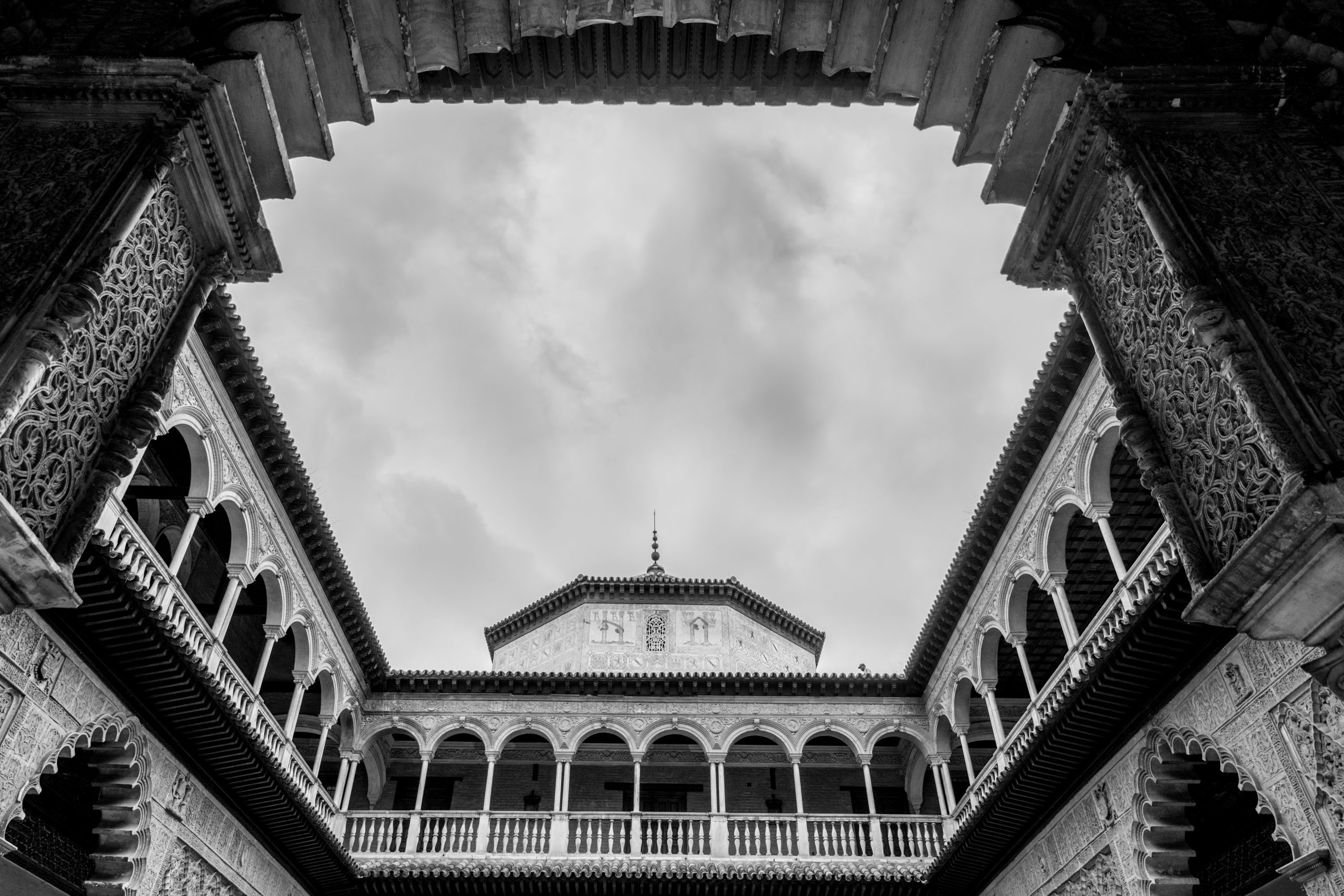 Black and white photograph of an open courtyard looking up inside the Alcazar of Seville.