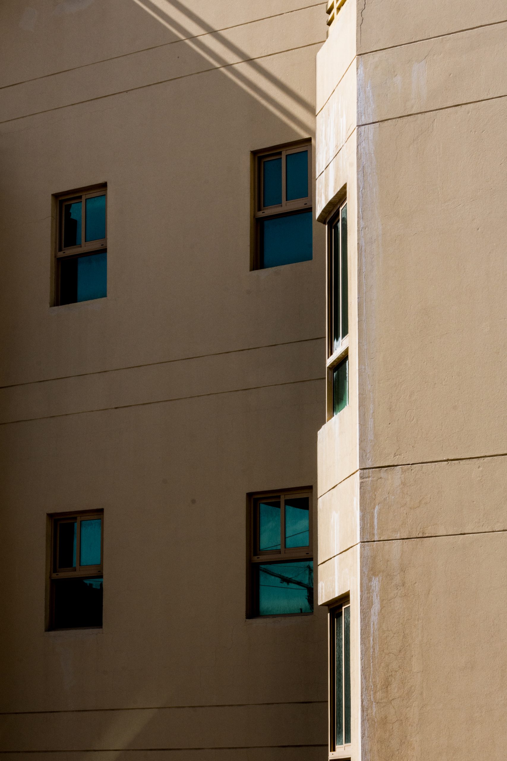 Photograph of the closeup of the face of a beige building with 4 green tinted windows