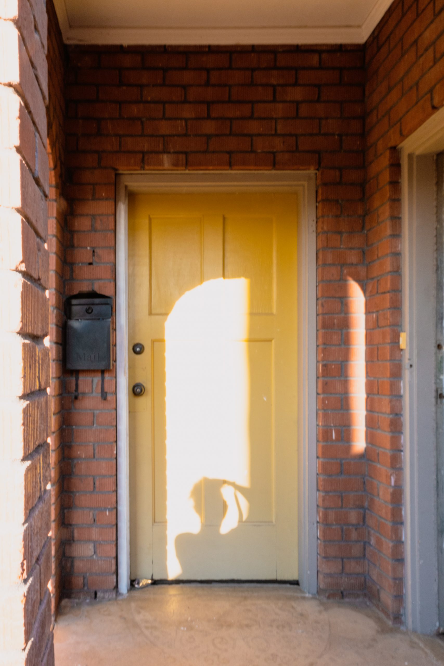 Photograph of a person's silhoutte as they take a photo in front of a yellow door surrounded by red bricks.